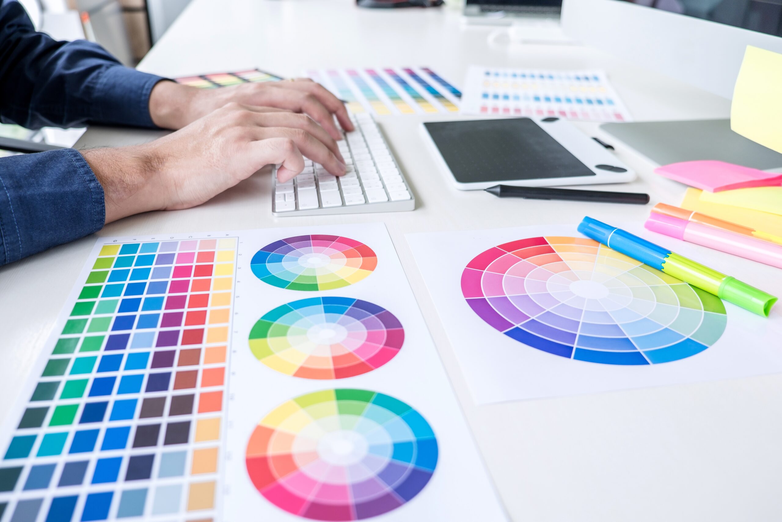 Image of male creative graphic designer working on color selection and drawing on graphics tablet at workplace with work tools and accessories.